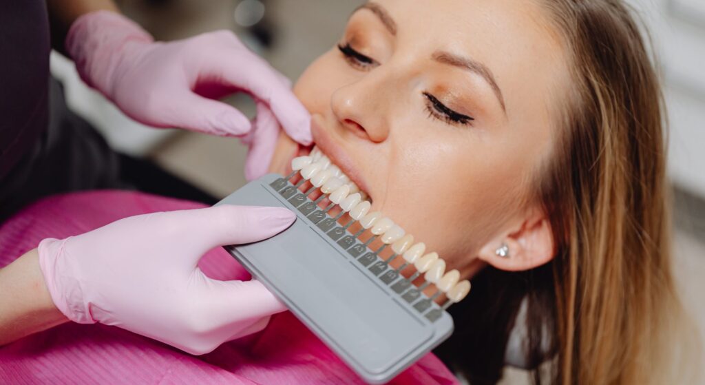 person wearing pink gloves holds a tooth shade test strips next to woman's teeth