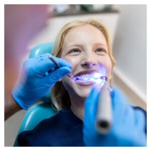 woman smiles in dentist chair with blue light near teeth 