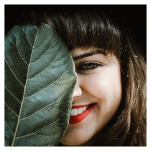 portrait photo of woman with red lipstick holding leaf over half of her face 