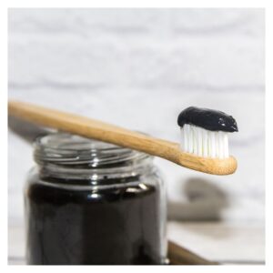 black charcoal toothpaste in a glass jar and on bamboo toothbrush