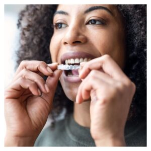 woman with curly hair holds a clear plastic mold of top teeth 