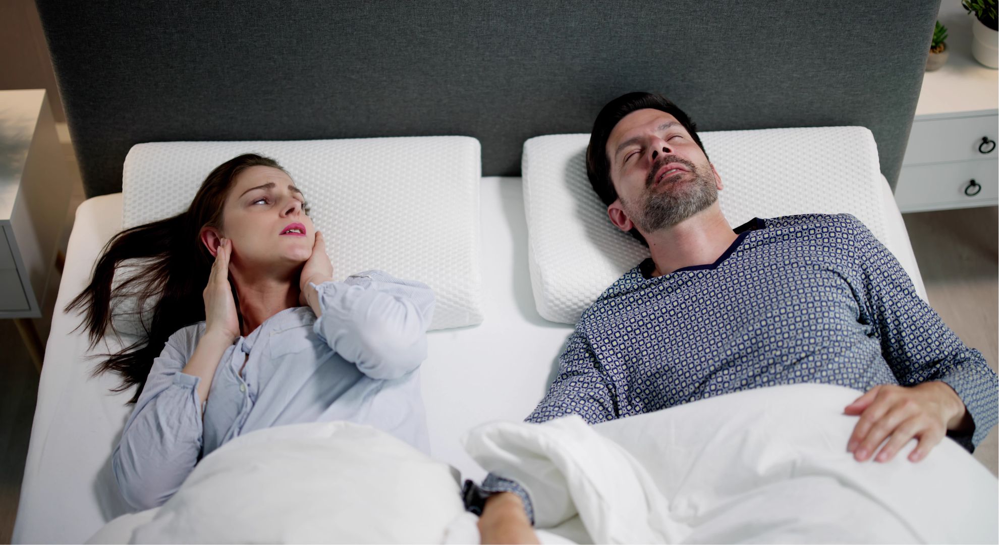 woman holds hands to ears while man snores beside her