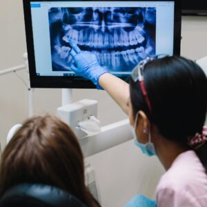 A dentist and a dental assistant are reviewing a patient's digital panoramic X-ray on a computer screen. They are pointing to the screen and discussing the results.