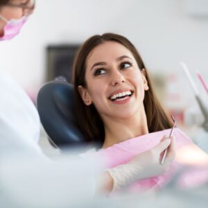 Female patient smiling widely and looking up at the dentist in a clean, modern operatory; represents trust and satisfaction with care.