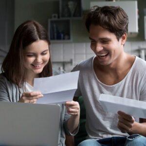 Young, smiling couple looking happily at financial paperwork or documents in their home, representing relief from financial worry.